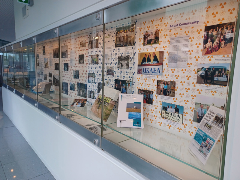 Glass cabinets filled with a display of community images at Nucleus. Images include pictures of Queen Elizabeth II, a copy of the NDA Socio-Economic Report, and a page from the local newspaper highlighting Nucleus staff.